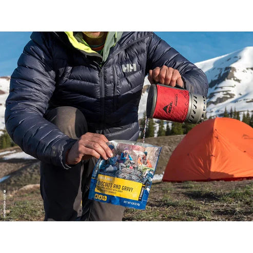 Person camping in mountains preparing food with a backpack and tent.