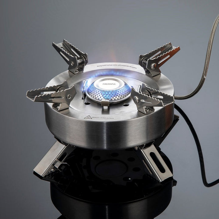 A portable gas stove with a blue flame, featuring a stainless steel body and foldable metal supports.