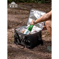 Person opening a black insulated cooler bag outdoors with a bottle inside.