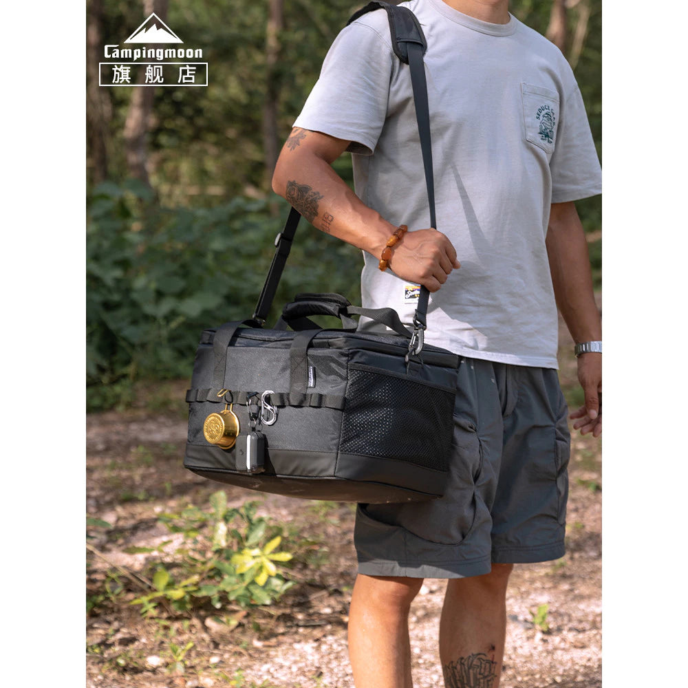 Person holding a black duffel bag outdoors with 'Campingmoon' branding.