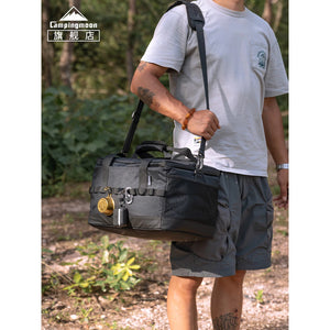 Person holding a black duffel bag outdoors with 'Campingmoon' branding.