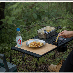 Camping scene with a portable table, food, and water bottle in a natural setting.