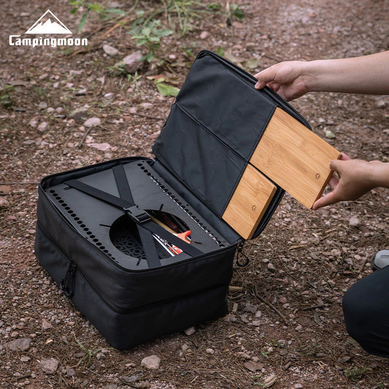 Person opening a black camping cooler with wooden cutting board on a natural ground background