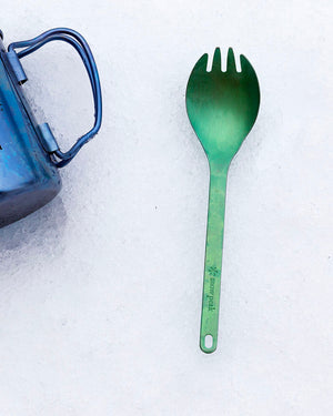 Snow Peak Titanium Spork SCT-004 in green resting on snow beside a blue titanium mug