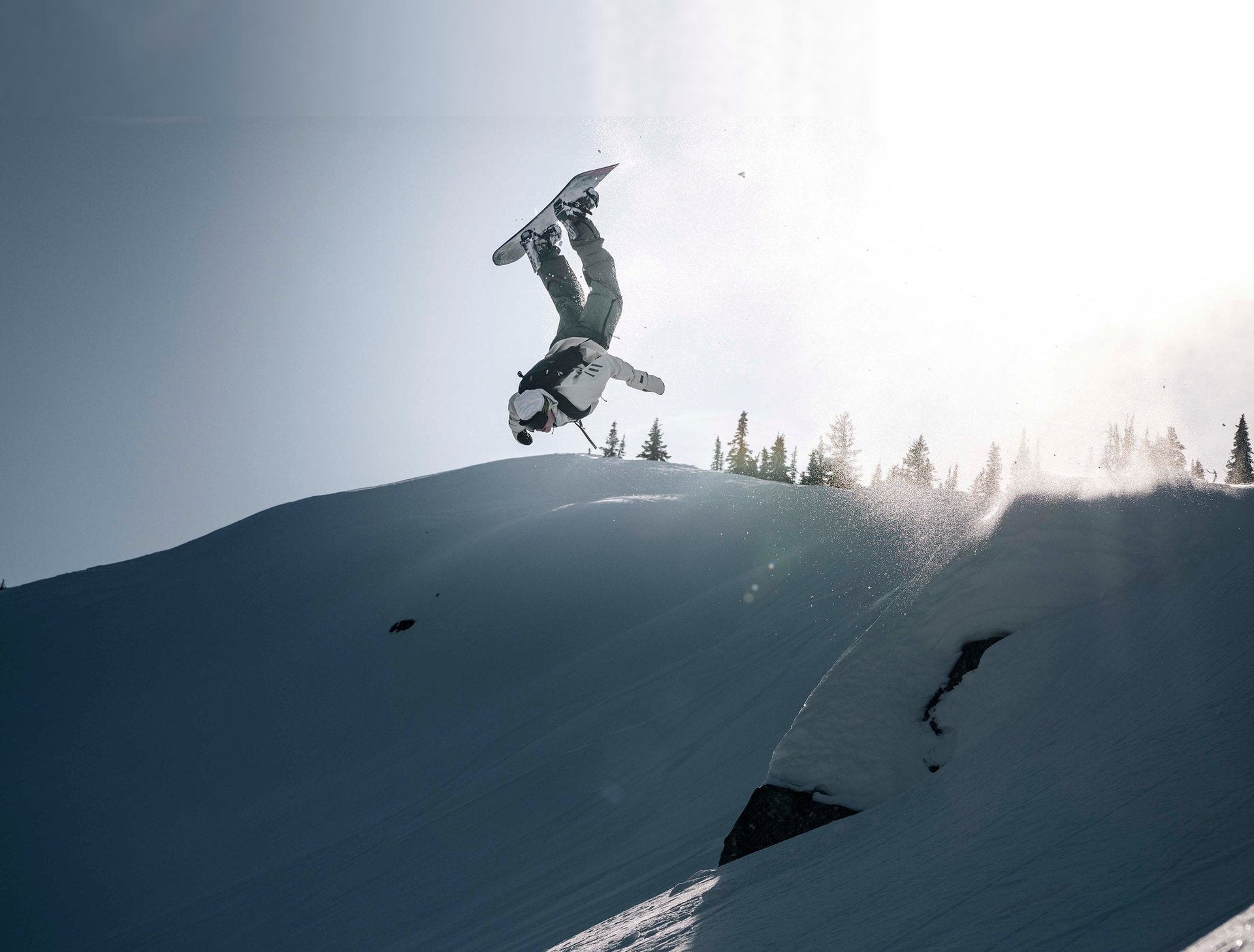 A snowboarder upside down above a sunlit ridge